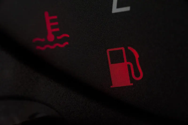 Fuel low warning lights illuminated on a car dashboard glowing in the darkness to indicate that it is time to stop and refuel