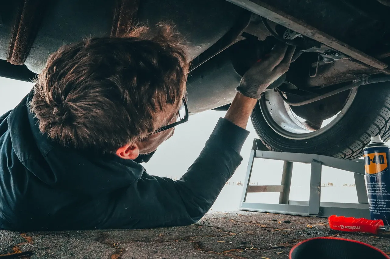 Image shows man performing DIY vehicle maintenance under his car.
